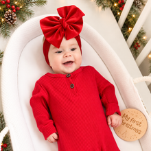 Load image into Gallery viewer, A baby wearing a festive red ribbed long-sleeve romper and matching red bow headband, lying in a white bassinet with Christmas decorations and a wooden 'My first Christmas' plaque nearby.